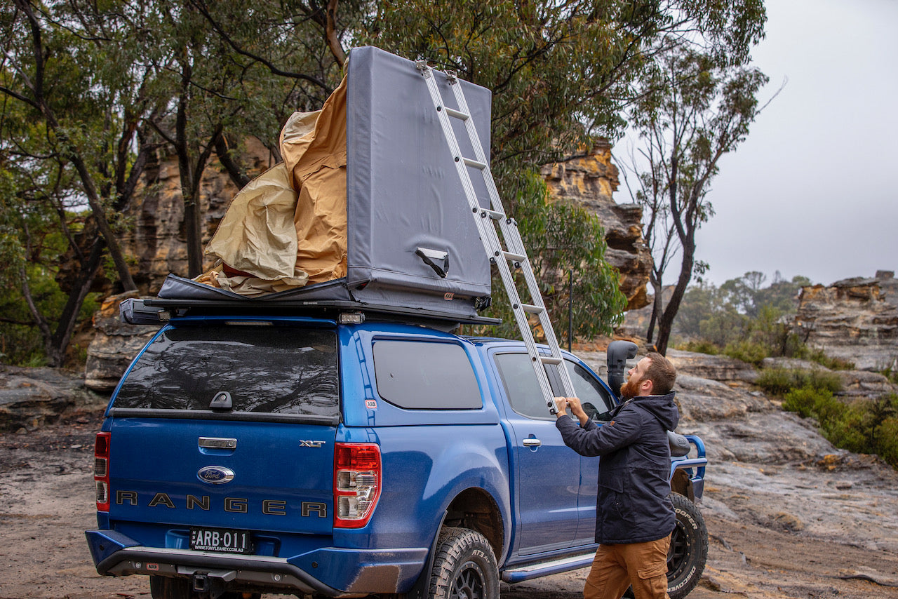 UN HOMBRE CERRANDO LA TIENDA DE TECHO FLINDERS DE ARB FIJO EN UN FORD RANGER BLEUE