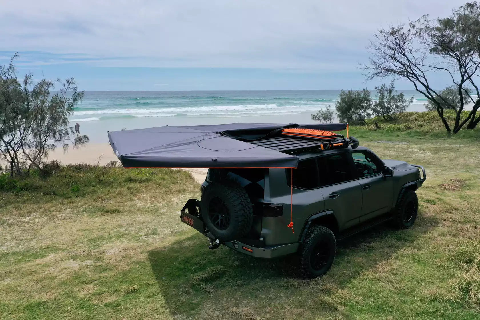 Toldo circular negro y naranja desplegado a la izquierda de un 4x4