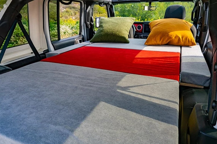 colchón gris y rojo en una furgoneta con 2 almohadas