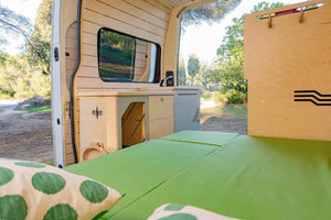 cama totalmente desplegada con colchón verde en una furgoneta transformada