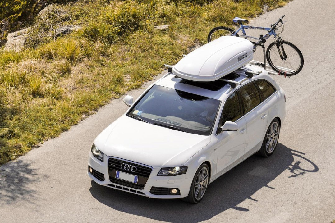 Audi blanco con una caja de techo blanca y una bicicleta detrás