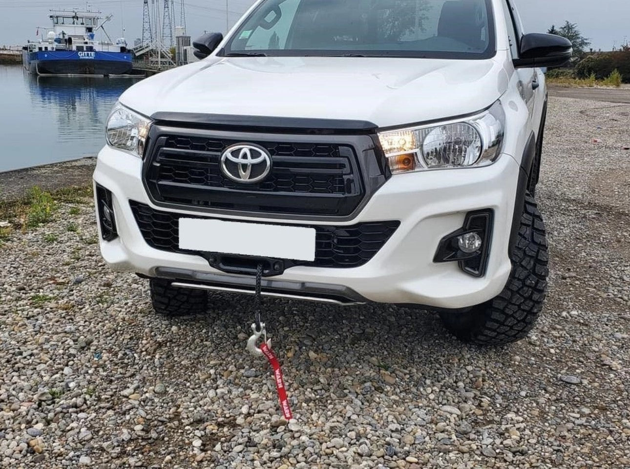 Toyota blanco delante de un barco con un cable que sobresale