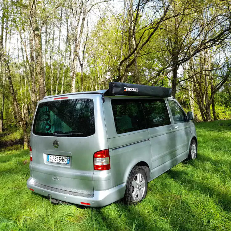 Volkswagen Transporter gris aparcado sobre la hierba con un Toldo cerrado y ordenado